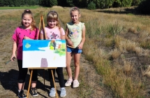 Trzy dziewczynki na polu stojące przy obrazach na sztaludze 