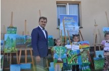 Mężczyzna i dwie dziewczynki z obrazami. W tle wystawa rysunków na sztalugach 