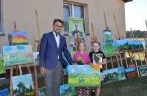 Dwie dziewczynki z obrazem i upominkami, obok nich mężczyzna 
