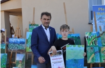 Chłopiec z obrazem i dyplomem na tle wystawy obrazów. Chłopiec trzyma dyplom i obraz 