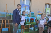 Mężczyzna i dziewczynka na tle obrazów. Obok inne dzieci. Wszyscy stoją na tle wystawy obrazów 