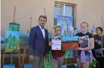 Dwie uśmiechnięte dziewczynki wraz mężczyzną. Dziewczynki trzymają dyplom oraz dyplomy 