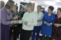 Kobieta podająca dłoń innej kobiecie, w tle inne osoby 