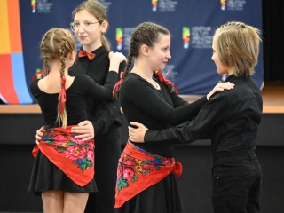 Dwie dziewczynki i dwoje chłopców tańczących w parach w jednakowych strojach